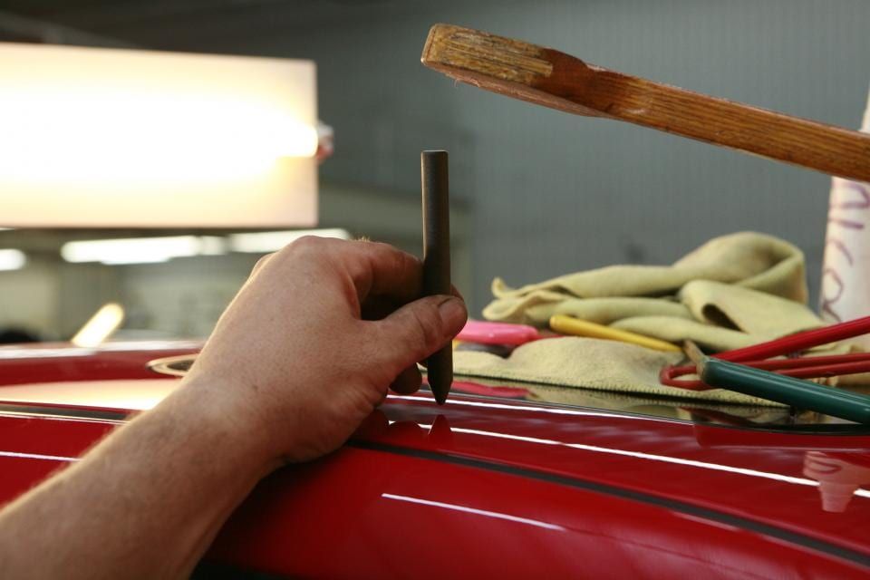 A gloved hand working a tool along the trim of a red car